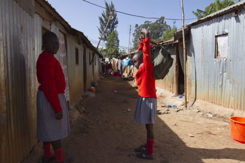 Two girls in school uniforms standing in a street in a slum